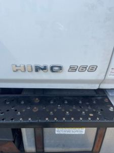 Hino 268 badge on rear door of box truck with black step below and metal surface.