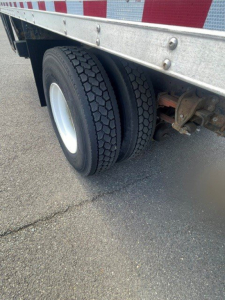 Rear wheel assembly of a box van truck showing dual tires and metal underride guard with reflective side rails.