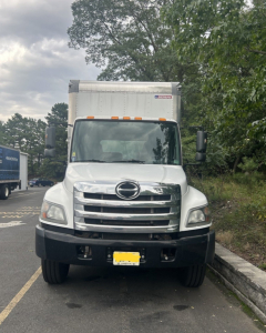Front view of a white 2019 Hino 268 box truck showing large chrome grille, Hino emblem, and rectangular cargo box; black bumper and mirrors visible.