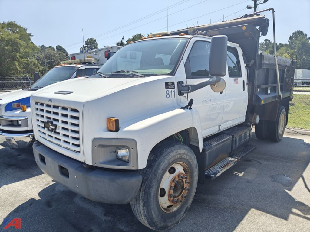 Truck: white 2005 Chevrolet C85000 dump truck, side view, with dump bed raised in background, large side mirrors, front grille with Chevrolet emblem, light bar on cab, visible wheel with steel rim.