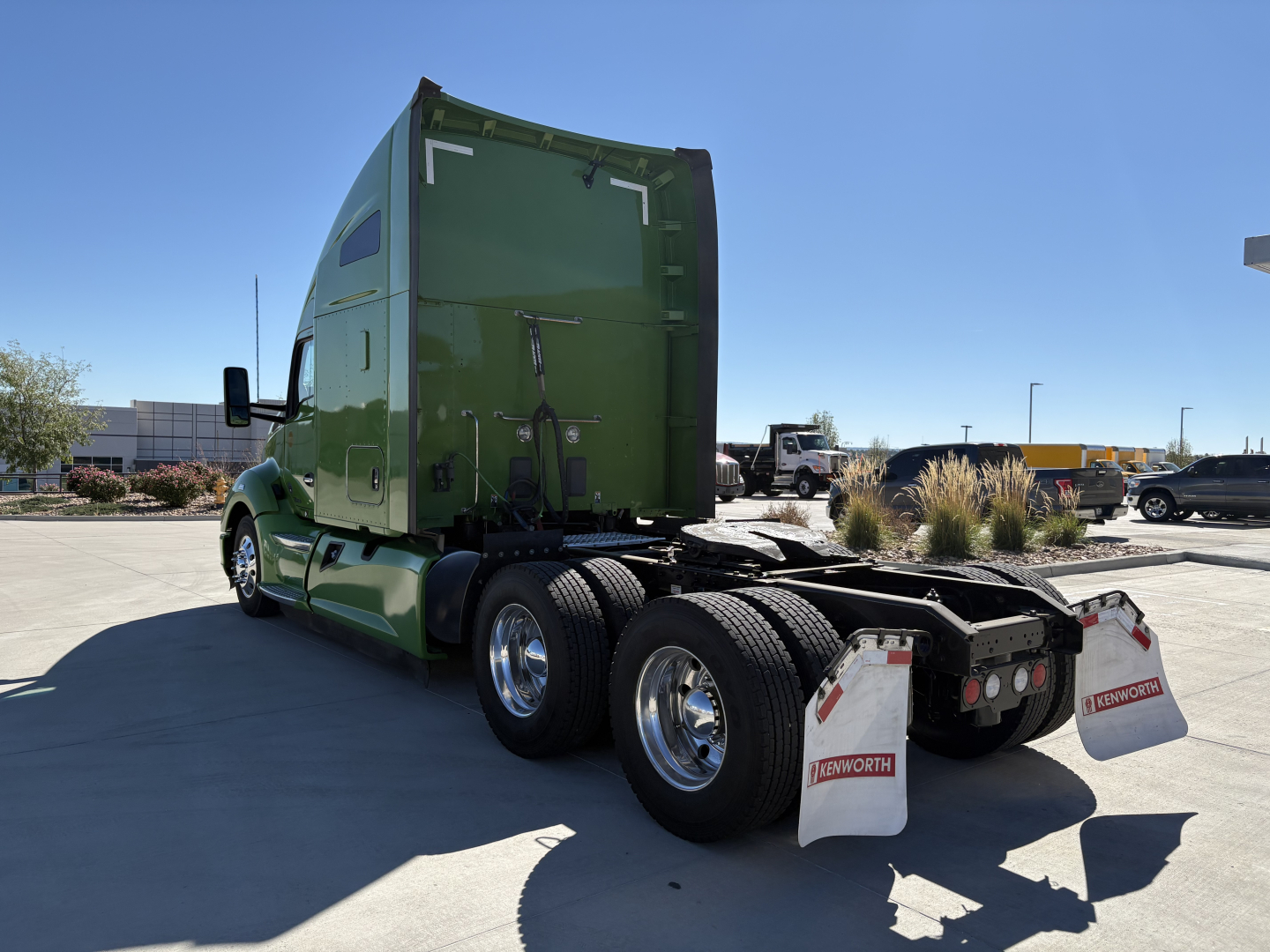 Kenworth T680 sleeper cab truck in green, rear three-quarter view showing dual rear axles and mud flaps with Hayworth branding, clear blue sky.