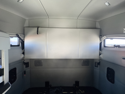 Kenworth T680 cab interior with sleeper and storage cabinet, light gray walls, small windows on sides, and overhead lighting.