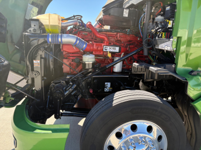 Kenworth T680 engine bay showing Cummins X15 engine label and blue radiator hose with green cab visible
