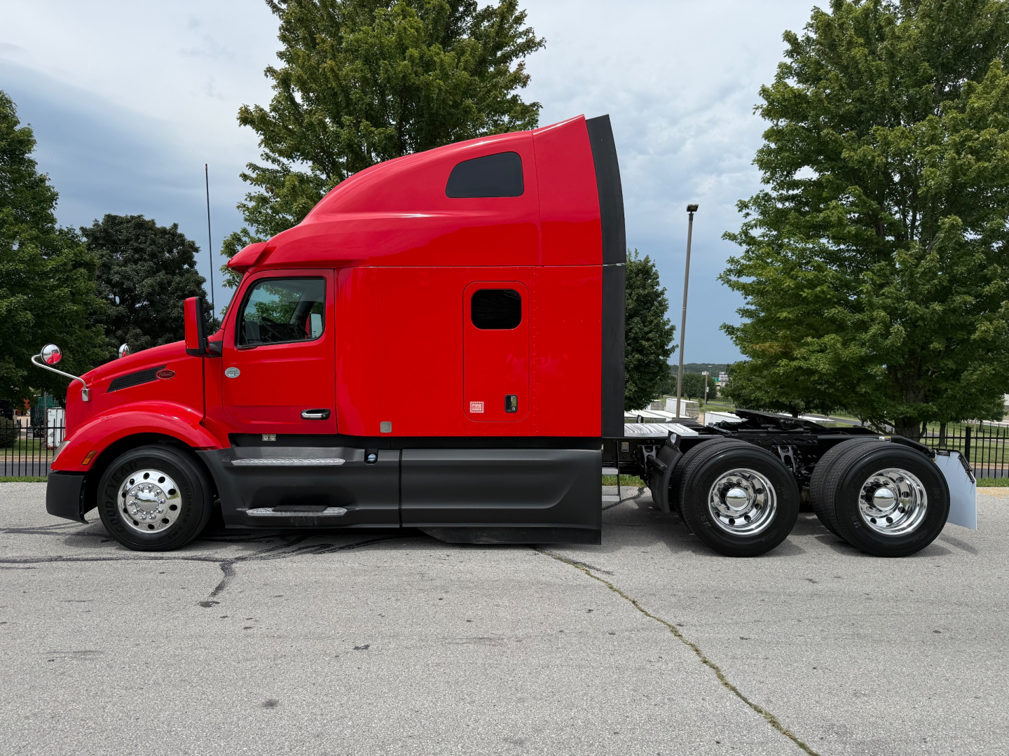 Truck side view showing a red 2023 Peterbilt 579 with sleeper cab in a parking lot.