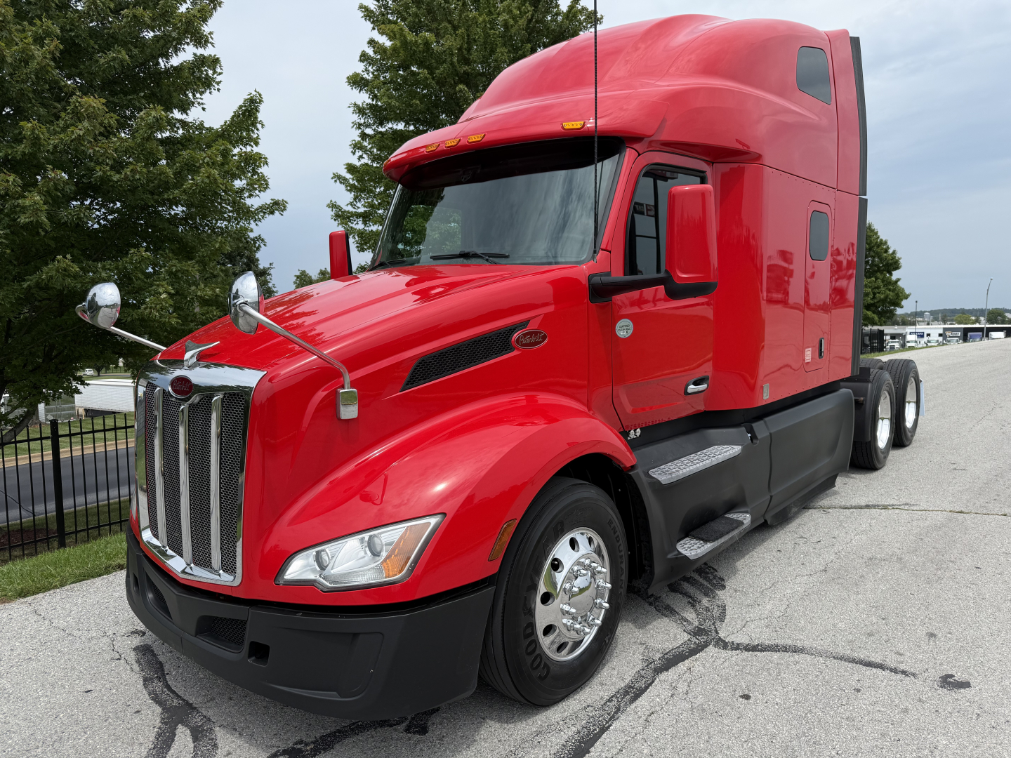 2023 Peterbilt 579 conventional sleeper truck in red, front-right view, chrome grille, dual mirrors, fuel tanks, black bumper, parked on pavement.
