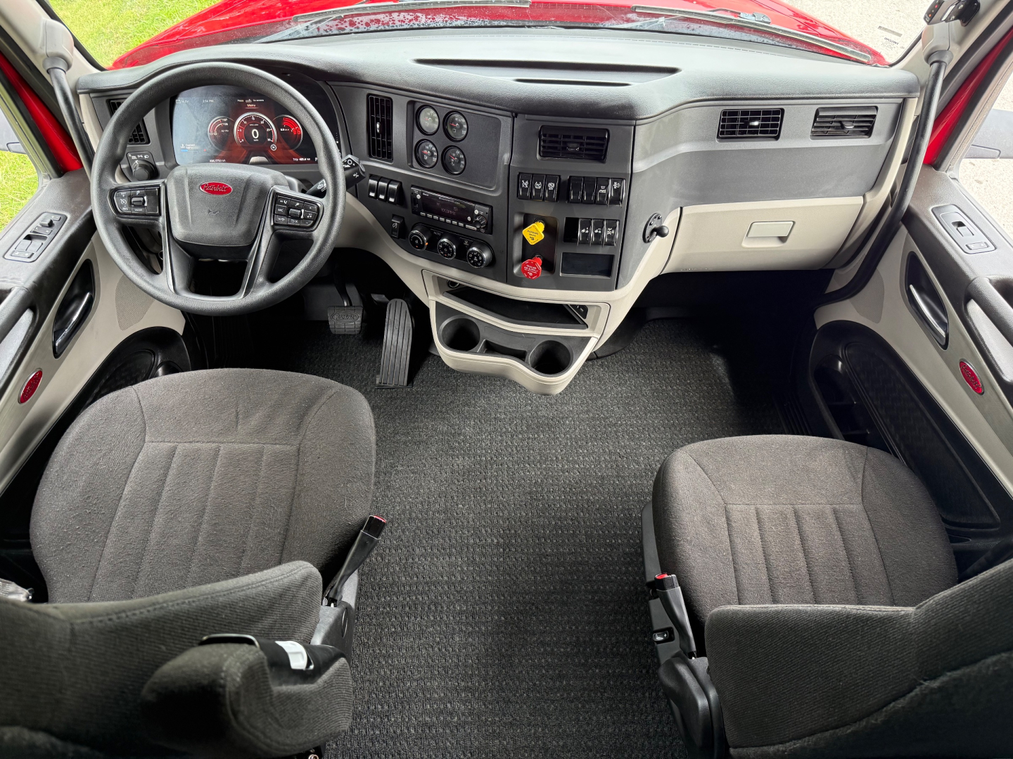 Cab interior of a Peterbilt 579 truck showing steering wheel, dashboard with gauges, center console, gear shifter, pedals, and two front seats.
