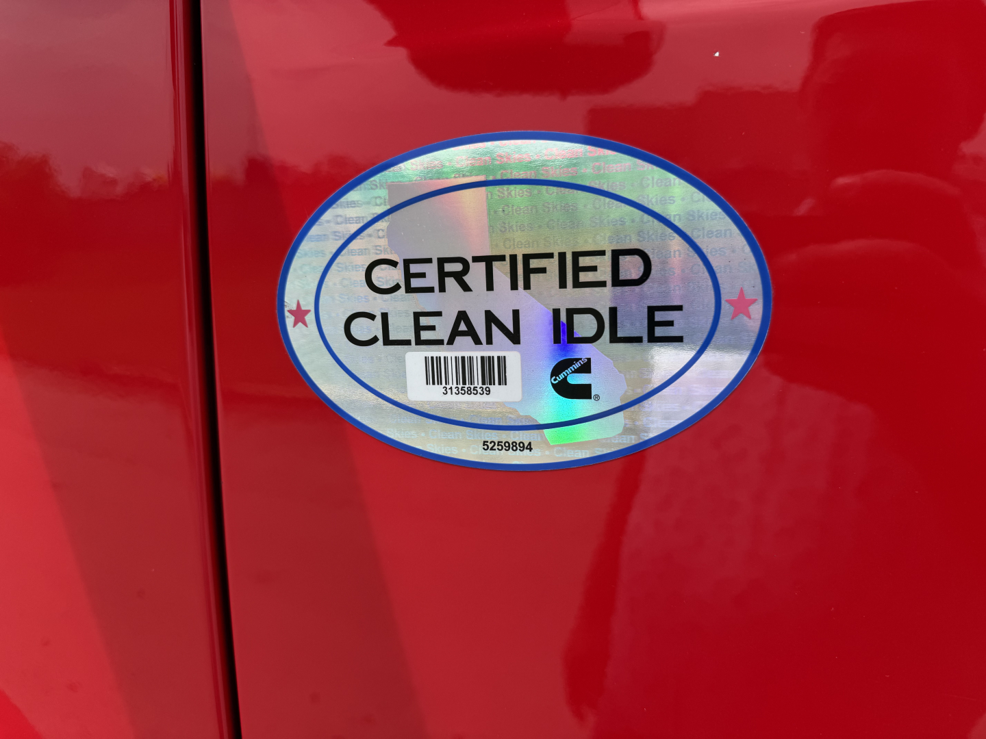 Sticker on red Peterbilt 579 door reading CERTIFIED CLEAN IDLE with holographic oval border and barcode.