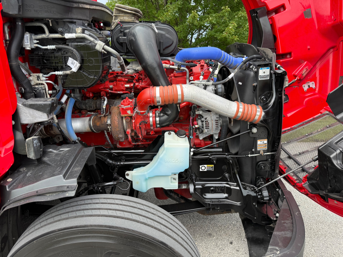 Peterbilt 579 engine bay showing diesel engine with red components, hoses, coolant reservoir, and radiator support.