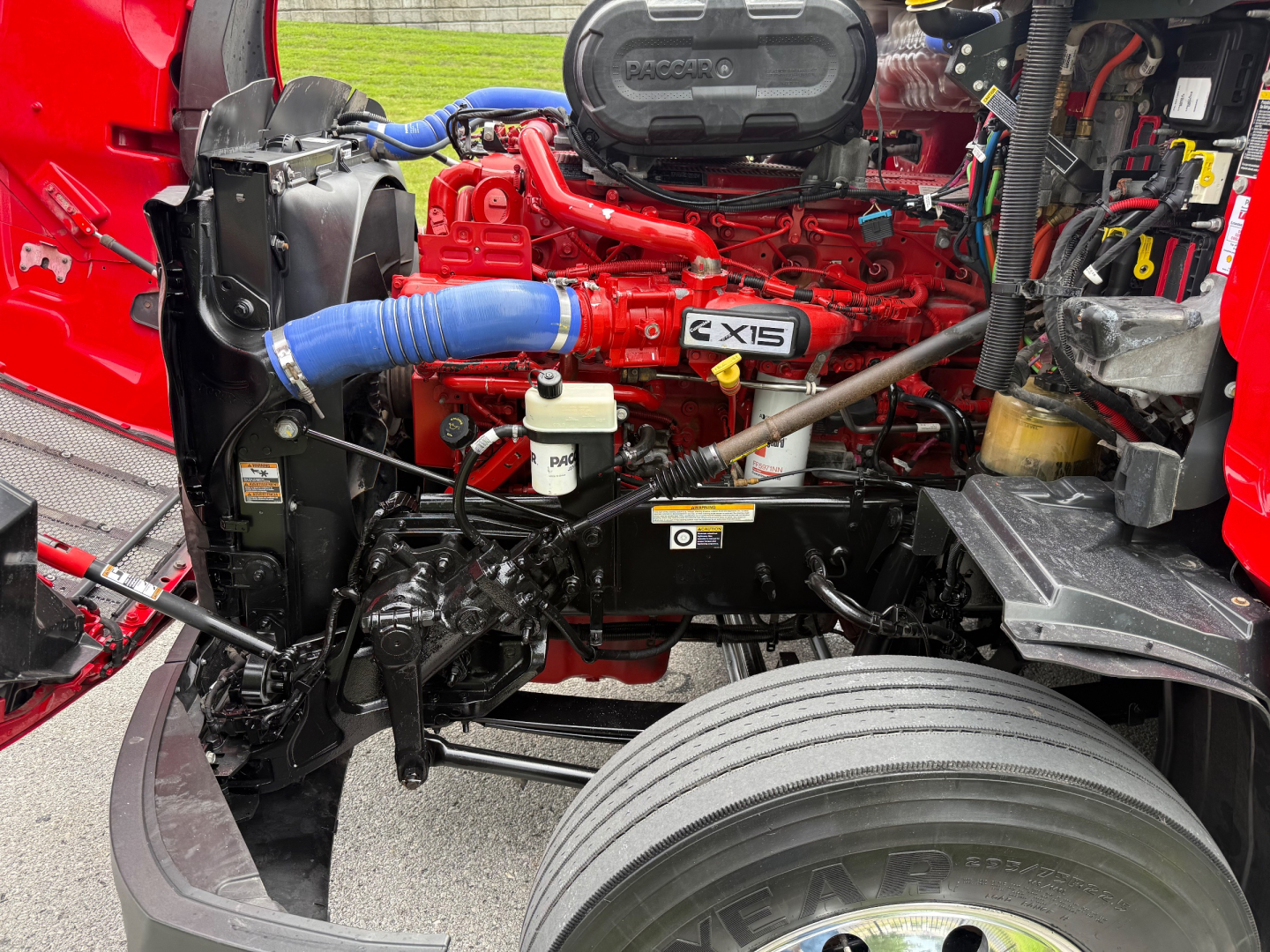 Peterbilt 579 engine bay showing Cummins X15 engine with red paint, blue silicone coolant hose, white reservoir, and various black hoses and components.