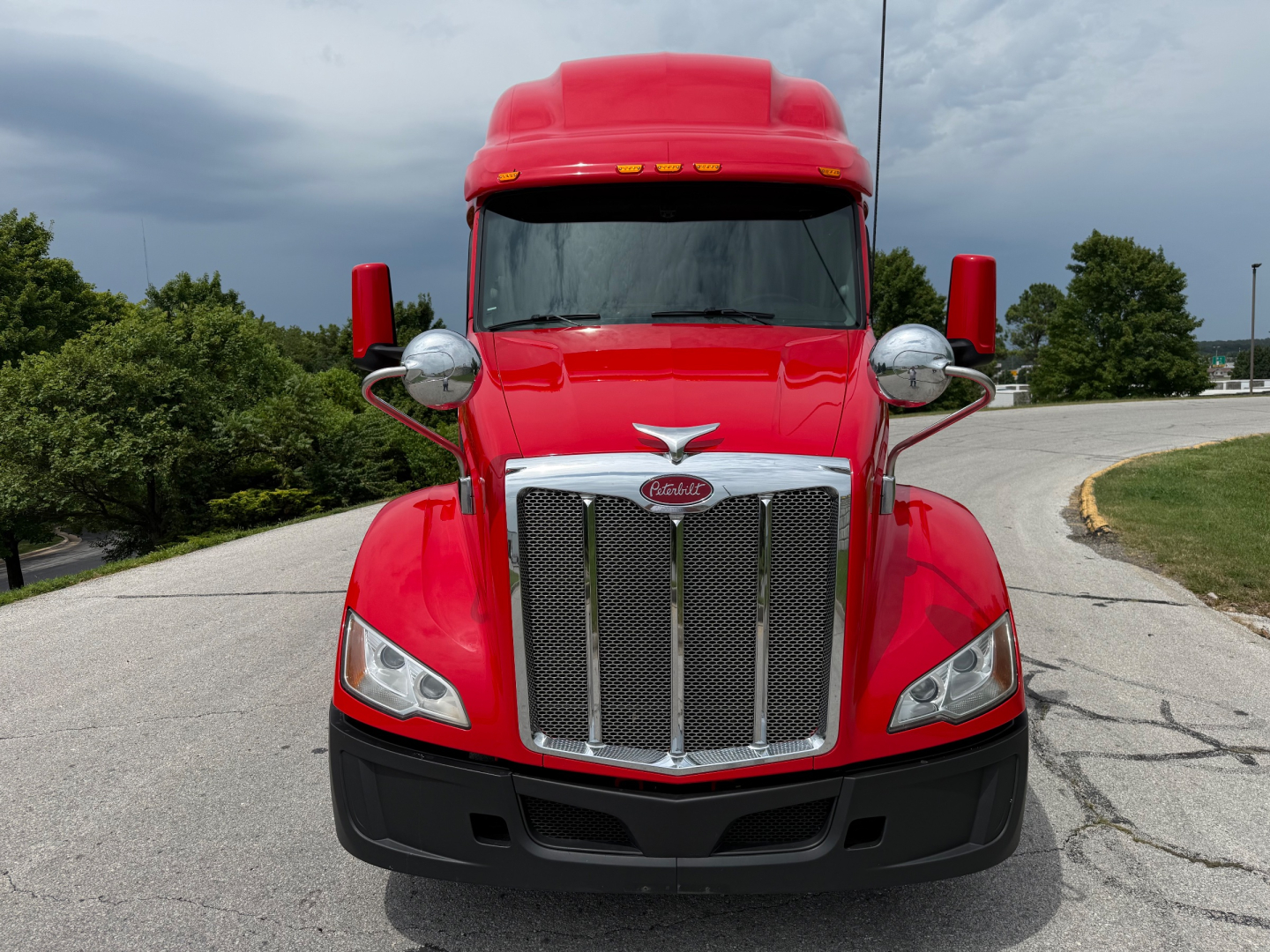 Peterbilt 579 conventional sleeper truck front view in red with chrome grille and logo, headlights, and side mirrors.