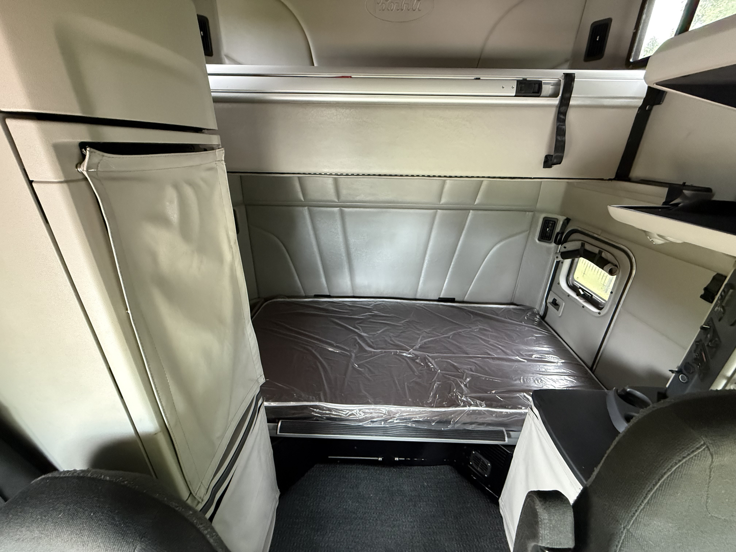 Peterbilt 579 sleeper cab interior showing a folded-in-bed bunk area, storage compartments, and beige panels.