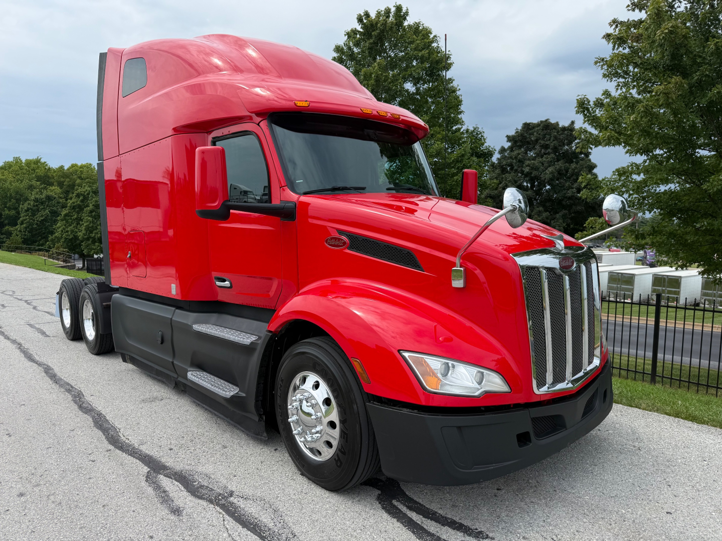 Peterbilt 579 tractor with red cab, sleeper, and chrome grille in a dealership lot.