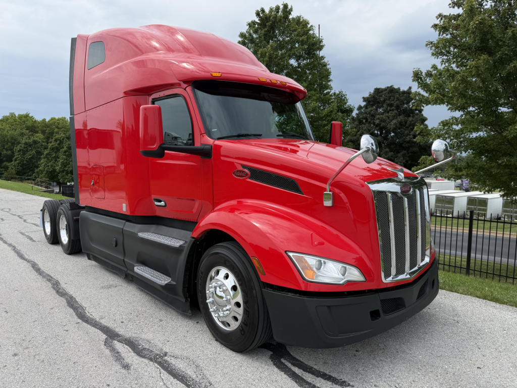 Red Peterbilt 579 tractor-trailer in a parking lot, side view with sleeper cab, chrome grille, and large mirrors.