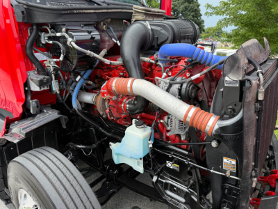 Vehicle engine bay of a 2023 Peterbilt 579 with red engine, large intake hose, blue hoses, and various components visible.