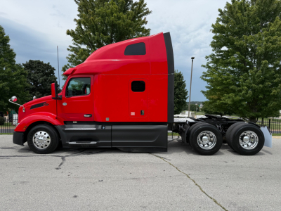 Truck side view showing a red 2023 Peterbilt 579 with sleeper cab in a parking lot.