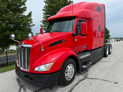 Peterbilt 579 conventional sleeper truck in red, front left view, large chrome grille, dual exhaust mirrors, sitting on road.