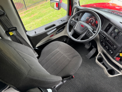 Peterbilt truck interior showing steering wheel with Peterbilt badge, dashboard with gauges, driver seat, door panel, and center console. Visible text includes no explicit model text, but interior controls and gauges are present.