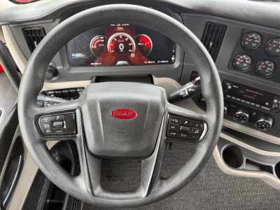 Peterbilt 579 interior steering wheel with digital gauge cluster showing red accents; steering wheel center badge Peterbilt; dashboard controls and gauges visible.