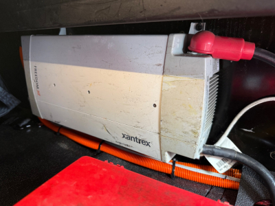 Xantrex inverter/charger mounted in truck cabin area with red battery terminal on top, orange cable loom nearby, some dirt and wear visible