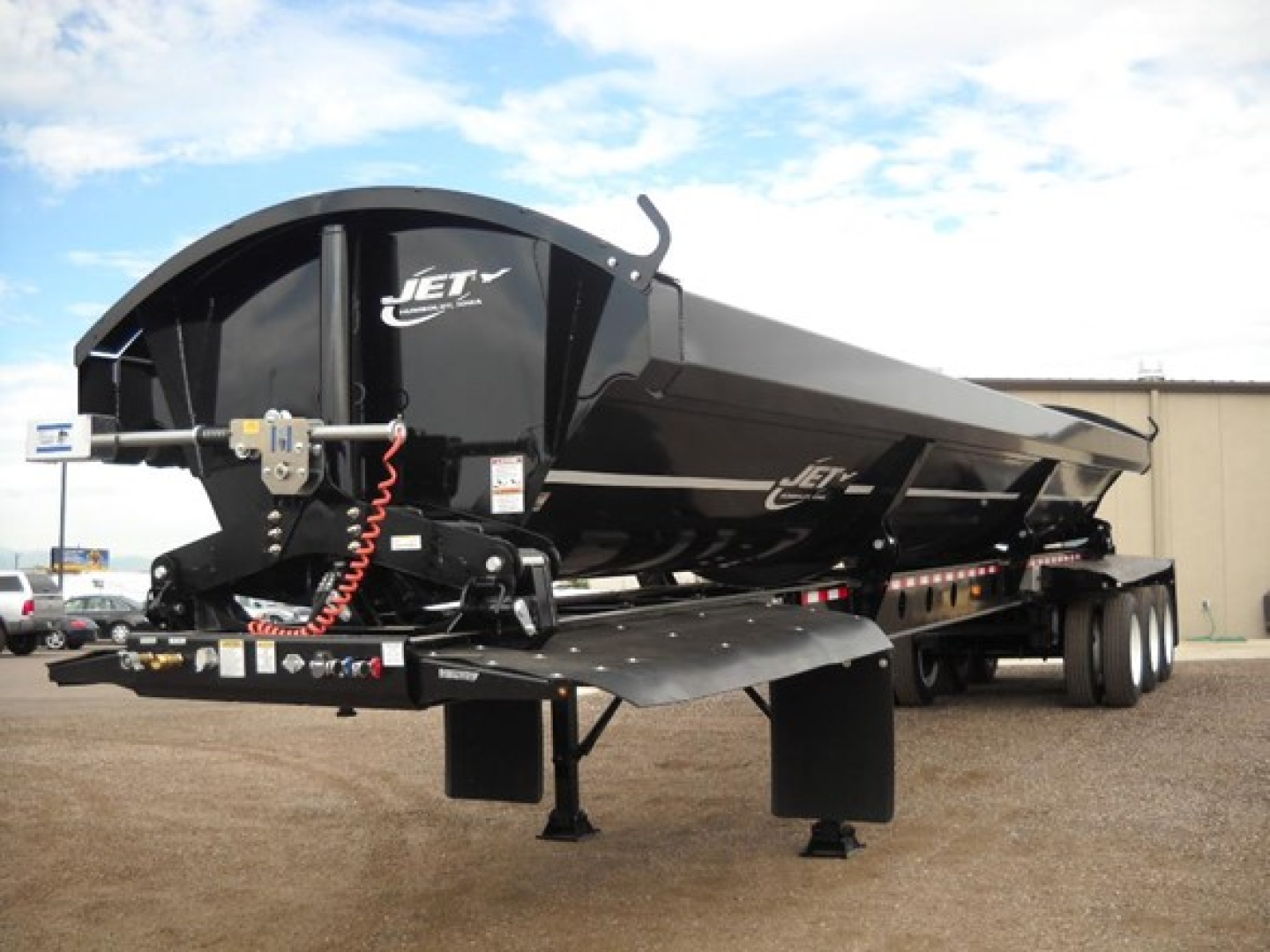 Jet Tri Axle Side Dump trailer showing Jet logo on black alloy hopper with hydraulic hoses and hitch, parked on lot.