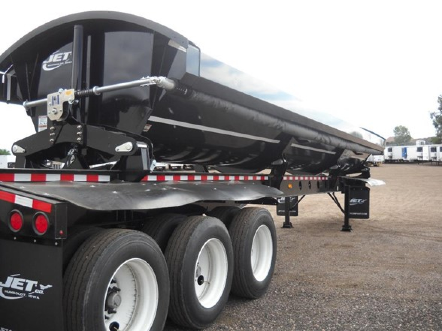 Jet tri-axle side dump trailer showing black dump body and triple axle with white wheels.