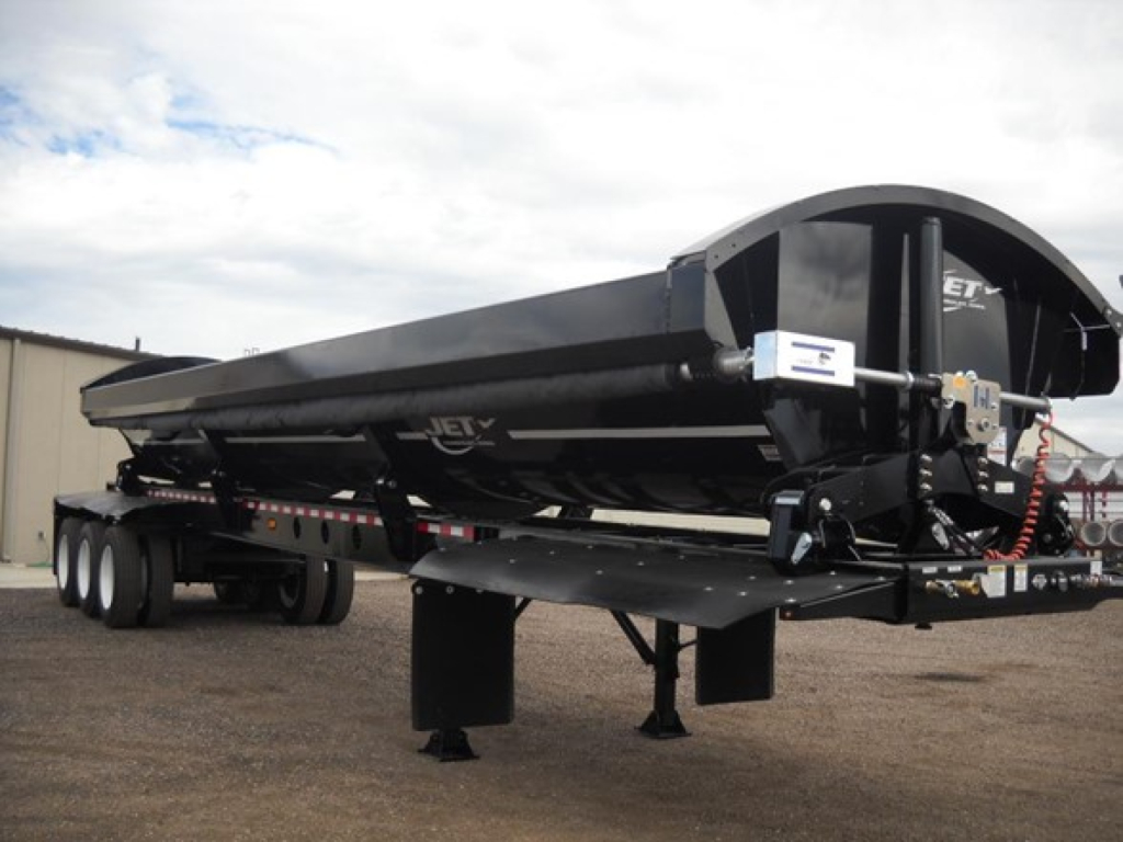 Tri-axle side dump trailer with black exterior, Jet brand, long rectangular hopper, landing gear down, front coupler and hoses visible.
