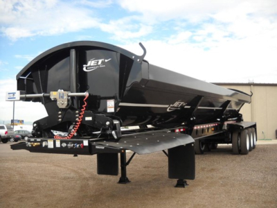 Jet Tri Axle Side Dump trailer showing Jet logo on black alloy hopper with hydraulic hoses and hitch, parked on lot.