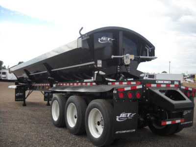 Tri-axle Jet side dump trailer on a flatbed with black and white color, Jet logo on the side, rear view showing triple axle wheels and tail area.