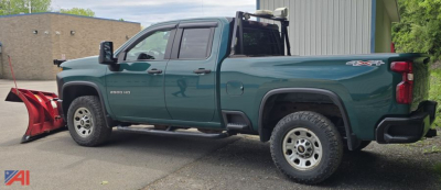 Chevrolet Silverado 2500HD Crew Cab pickup with plow attachment on front, teal green body, 4x4 badge, side steps, off-road tires, dealership lot.