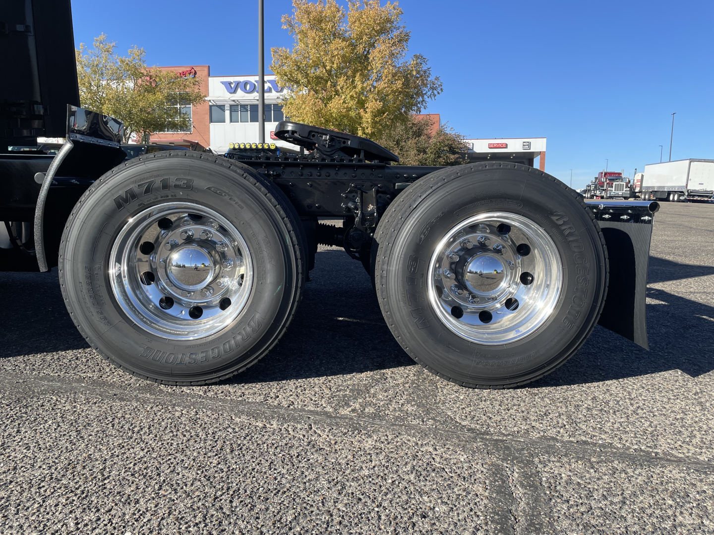 Dual rear tractor wheels and tires on a Volvo VNL64T660 truck chassis, chrome rims, black frame, sunny day in a dealership lot.