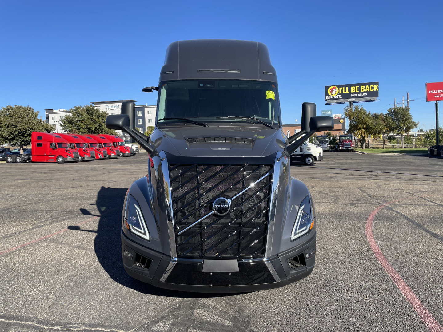 Front view of a dark Volvo VNL64T660 tractor in a dealership lot with other red trucks in background; grille, headlights, and Volvo emblem visible.