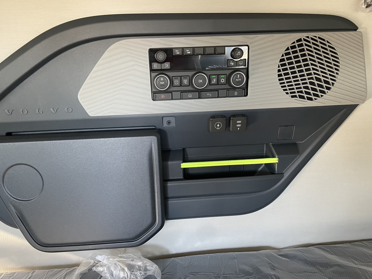 Volvo interior dashboard with control panel, speaker cover, and a neon green notebook or card in the lower pocket.