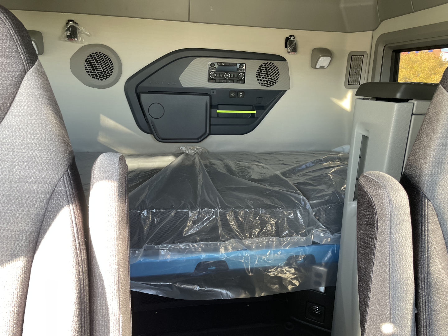 Volvo VNL64T660 sleeper cab interior showing control panel, storage pocket, two speaker grilles, and plastic-covered bunk area.