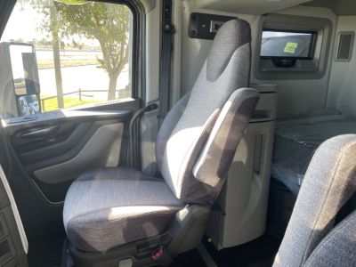Volvo VNL64T660 truck cab interior seating area showing driver seat and passenger seat, sleeper area in background with window and storage cabinet.