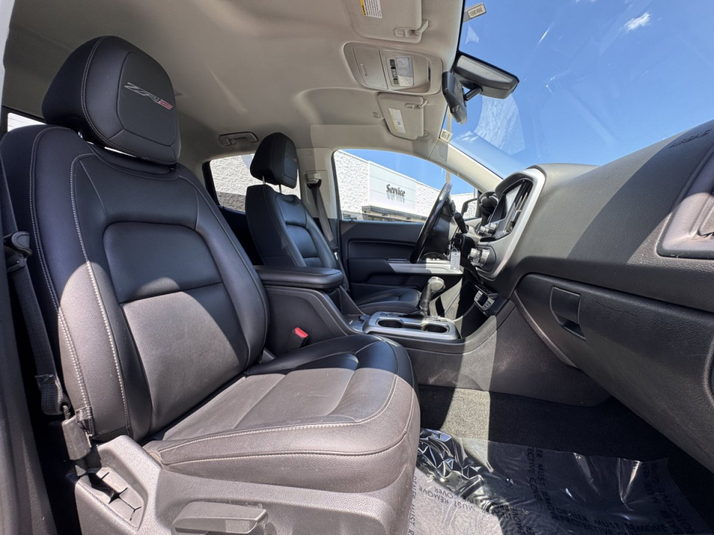 Interior view of 2018 Chevrolet Colorado front seats and dashboard from passenger side showing cloth and leather seats, center console, steering wheel, and front door panel.