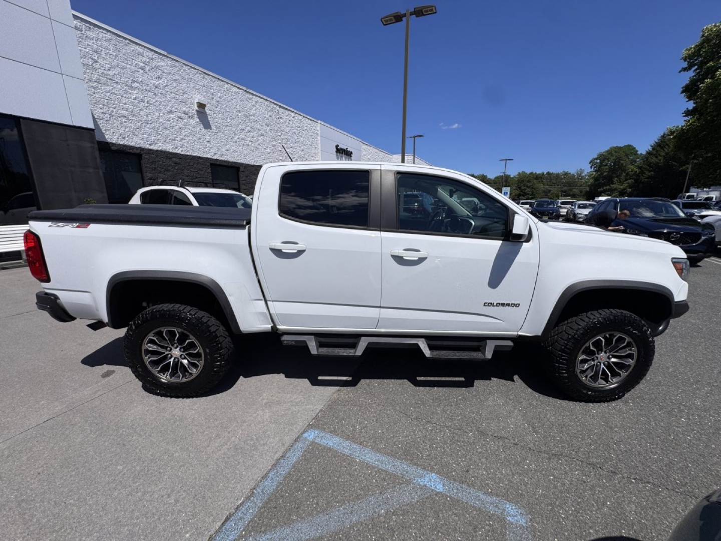 2018 Chevrolet Colorado pickup truck side view showing crew cab, white exterior, running boards, and bed with tonneau cover.