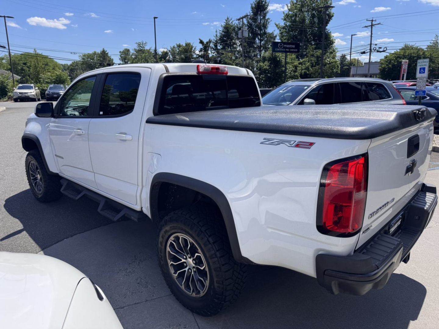 White 2018 Chevrolet Colorado Crew Cab Z71 LT pickup truck with bed cover parked in a lot, showing rear and passenger side.