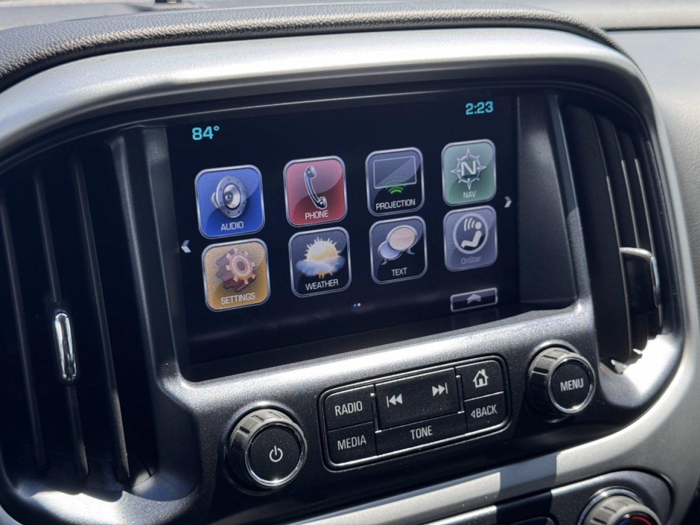 Chevrolet Colorado dashboard touchscreen display with icons for audio, phone, projection, navigation, settings, weather, text, and more; knobs for radio media tone and menu visible.