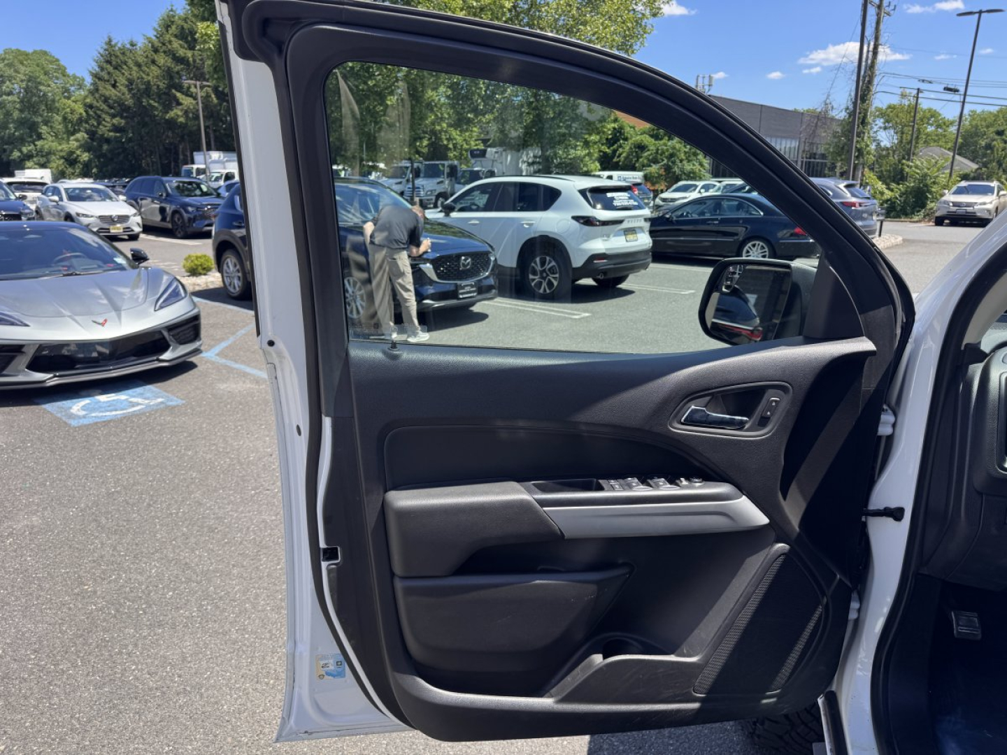 Front passenger door interior of a Chevrolet Colorado pickup with power window controls; side mirror and street scene visible through open door.