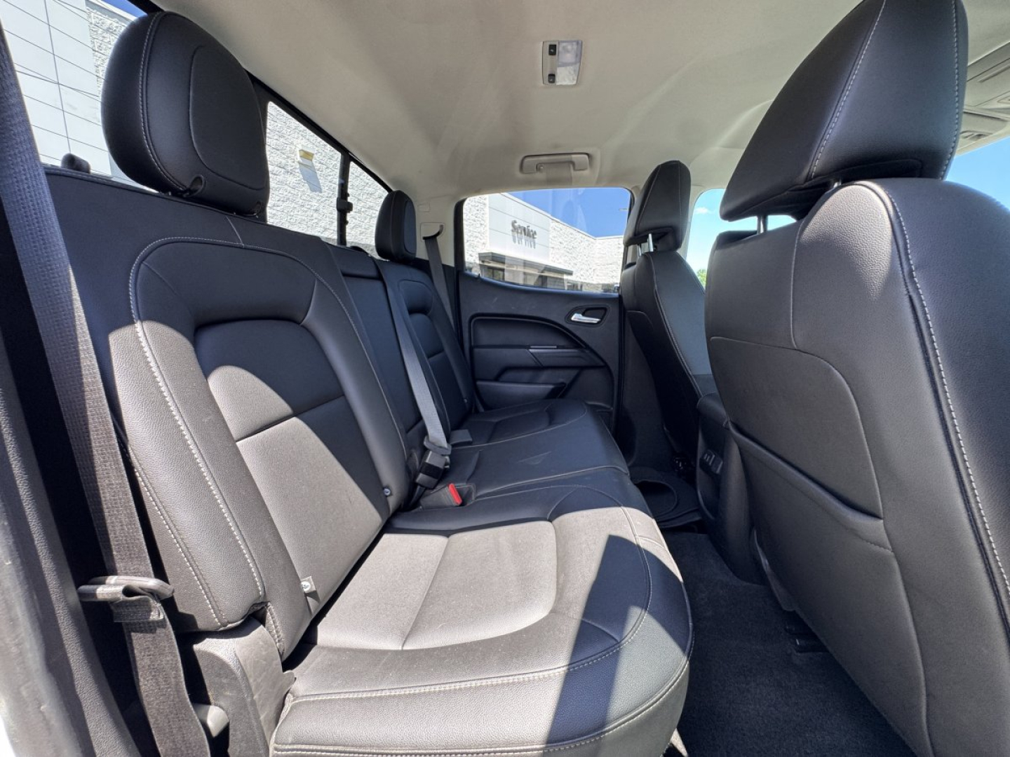 Chevrolet Colorado interior rear seating area showing gray cloth seats, rear bench with three seat belts, door panels, and front passenger seat in view.