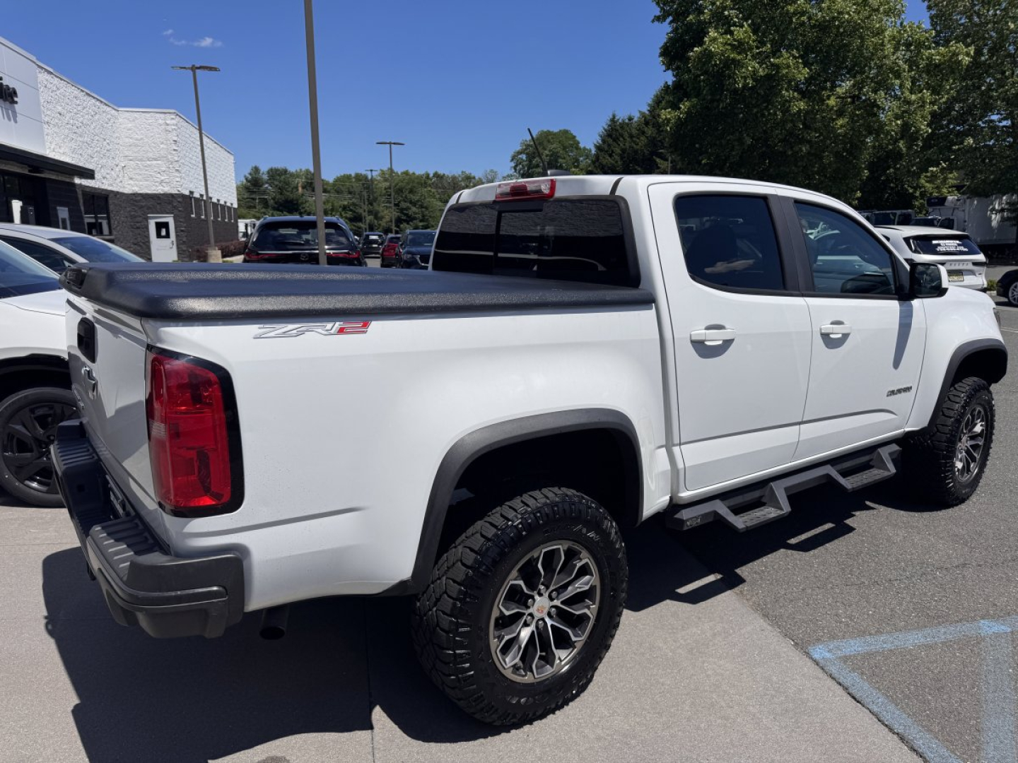 Chevrolet Colorado pickup truck rear-left side view showing crew cab, white paint, ZR2/4x4-style badges, bed cover, running boards, and off-road tires.
