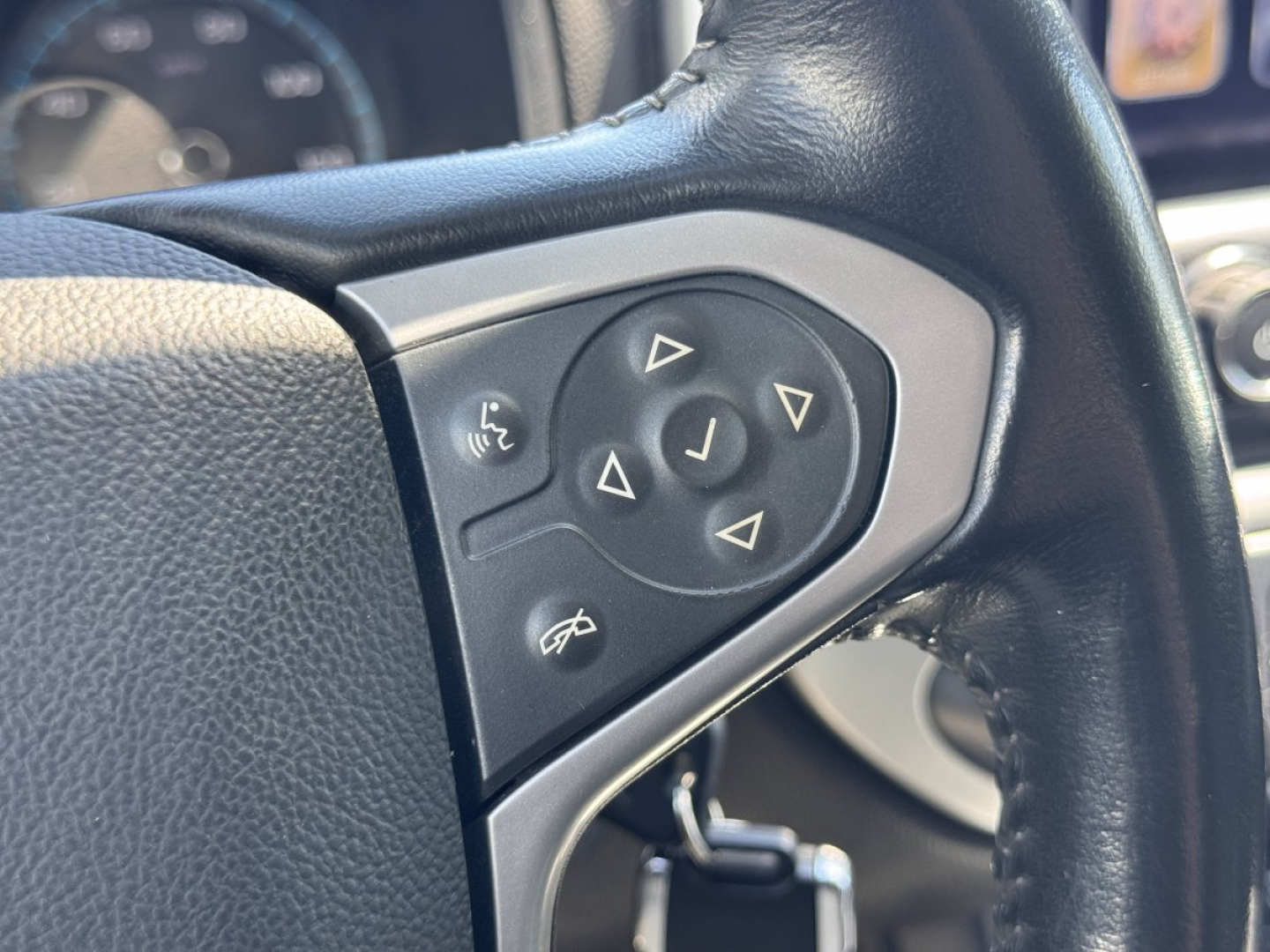 Steering wheel with control pad showing navigation arrows and phone icons on a Chevrolet Colorado interior.