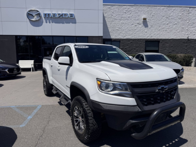 White 2018 Chevrolet Colorado pickup truck in dealership lot showing front bumper guard, black grille, and raised tires.