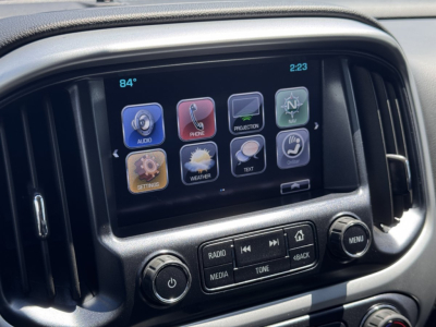 Chevrolet Colorado dashboard touchscreen display with icons for audio, phone, projection, navigation, settings, weather, text, and more; knobs for radio media tone and menu visible.