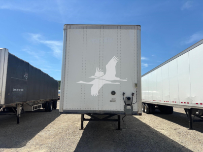 Trailer rear view showing a white bird decal on a plain gray trailer with support legs, surrounded by other trailers on gravel.