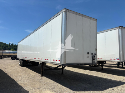 Trailer side view showing a white Vanguard VXP box trailer with undercarriage legs, no visible branding except shadowed logo, and daylight setting.