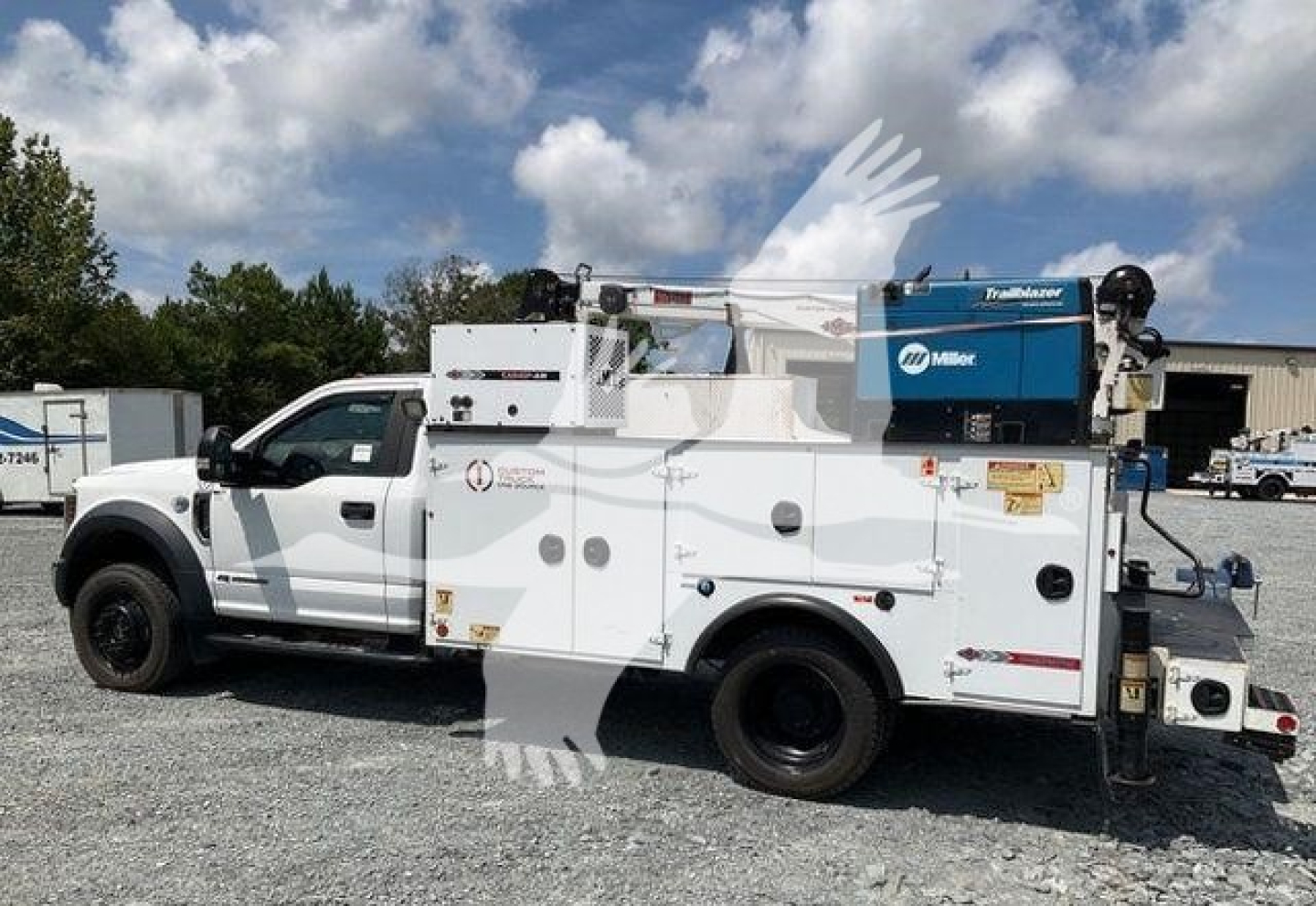 Ford F550 service/body truck with utility compartments, mounted Miller welder, and crane, side view showing work crew doors and storage, white paint.