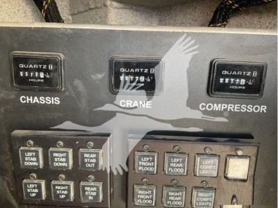 Panel showing gauges and switches in a Ford F-550 cab with 'CHASSIS' and 'CRANE' hour meters and multiple labeled controls.