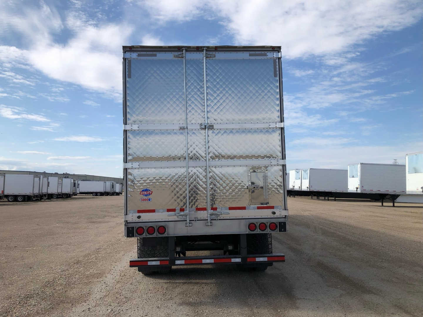 Rear view of a new Utility 3000R W trailer in a lot with diamond plate doors and taillights.