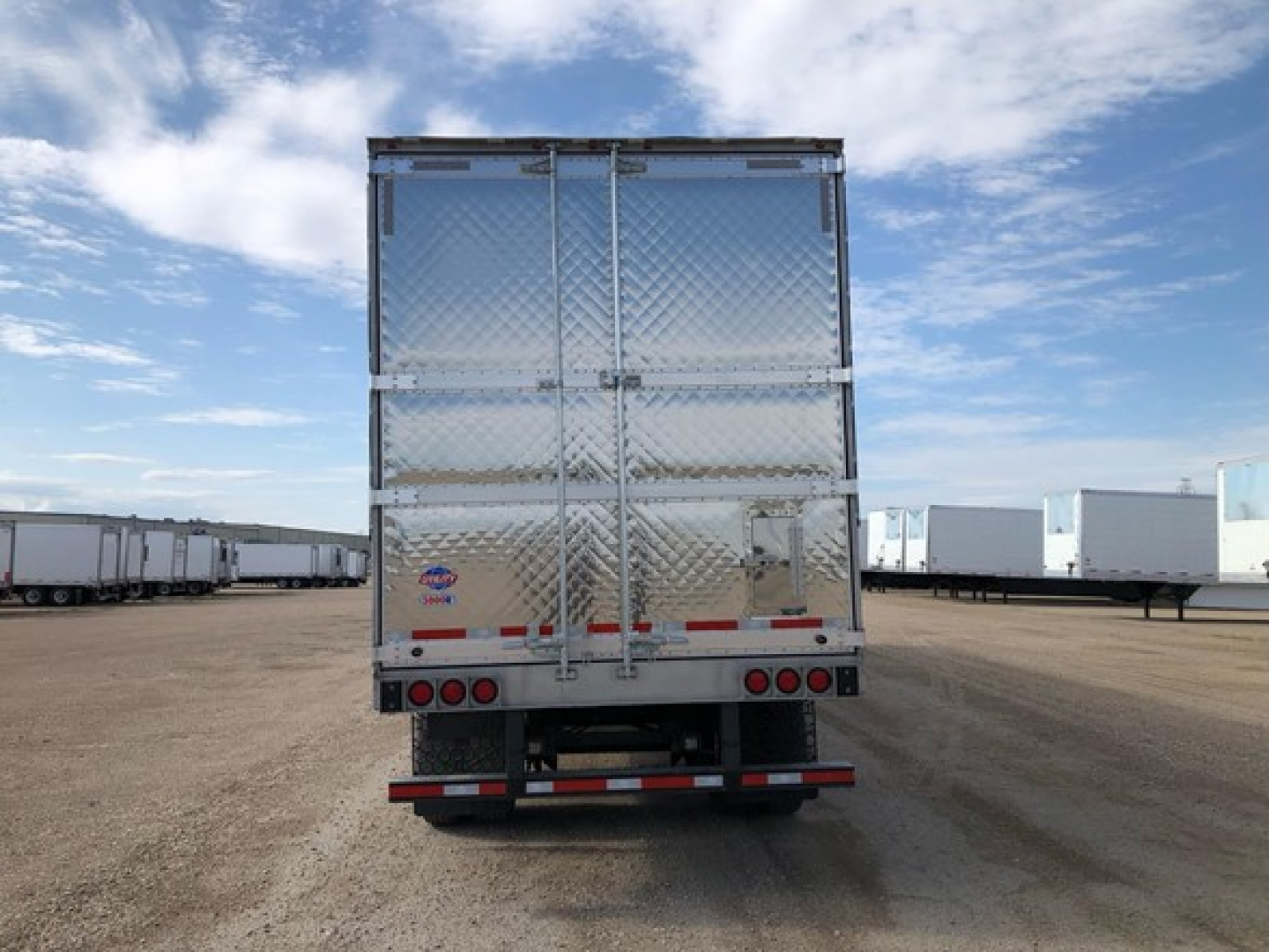 Rear view of a diamond-plate refrigerated trailer with Steel diamond plate doors, multiple lights, and bumper; manufacturer labels near lower left of rear doors.